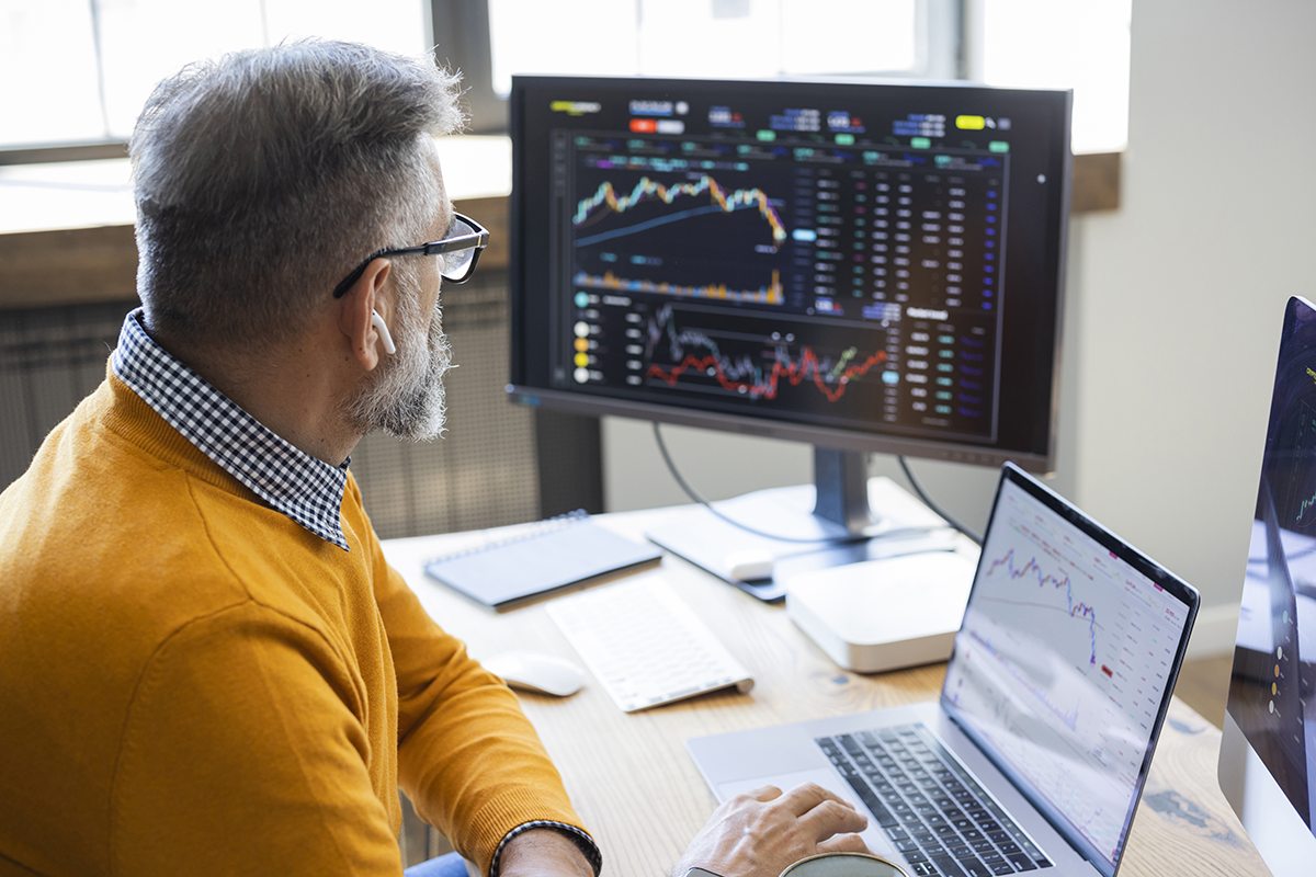 Man at desk looking at computer screens that are displaying graphs 