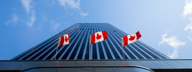 Tall building receding towards the sky with Canadian flags in the foreground