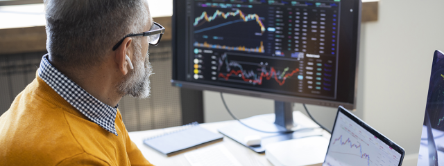 Man at desk looking at computer screens that are displaying graphs 