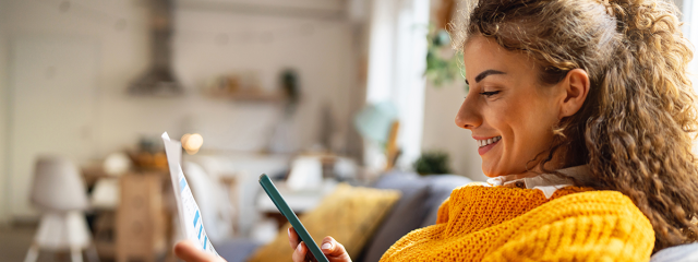Smiling woman with phone and paper invoice in her hands